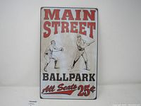 White metal sign with baseball graphics and text 'Main Street Ballpark All Seats 25¢'. Sign shows signs of age and wear.
