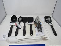 Full set of new kitchen utensils arranged in a row showing ladle, spatulas, tongs, and stirring spoons.