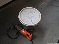 Electric saw next to plastic bucket labeled 'Rock Salt', both items on a concrete floor.