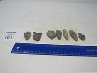 Seven stone arrowheads of various sizes and shapes laid out next to a ruler for scale