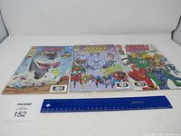 Front view of three Justice League comic books laid out with a ruler for scale