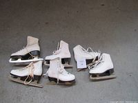 Three pairs of white figure skates arranged on the floor showing overall condition and sizes.