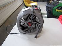 Front view of gray Vornado heater fan showing spiral protective grille and attached power cord with plug.