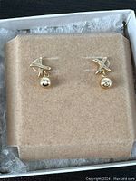 Pair of small 14K yellow gold earrings displayed on beige felt padding inside an open jewelry box.