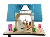 Front view of the Little Tikes dollhouse showing blue roof, beige walls with stone texture, staircase, balcony, and accessories including three figurines, pink stroller, trash bin, and plant decorations.