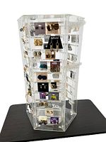 Front and side view of the clear six-sided acrylic jewelry display stand with multiple pairs of fashion earrings on cards attached to slots. Stand is placed on a black surface.