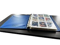 Open blue three-ring binder with plastic sleeves holding trading cards visible inside, angled shot showing binder wear.