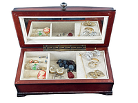 Wooden jewelry box opened showing glass-topped lid with mirror and an assortment of various costume jewelry inside divided compartments including cameo earrings, rings, beaded necklace, clip-on earrings, and stick pins.