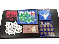 Coins and token sets displayed on a black table as lot contents, including Canadian portrait map coin set, US coin set, Canadian floral tokens and loose coins in sleeves.