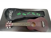 Full view of Denver ukulele along with its black embroidered soft carry case on a dark surface