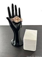Rose gold toned ladies analog watch displayed on a black hand stand beside closed white U.S. Polo Assn. branded box.