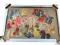 Wide view of all paper dolls and clothing pieces laid out inside a white tray showing full lot contents.