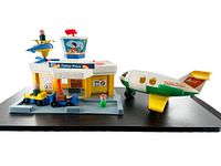 Front view of Fisher Price Play Family Jetport Airport toy set with airplane, helicopter, vehicle with luggage, and Little People figures displayed on black backdrop.
