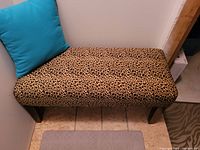 Rectangular bench with animal print fabric and wooden legs. Includes blue pillow placed on the bench.