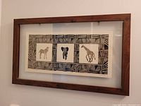 Framed triptych artwork displaying zebra, elephant, and giraffe illustrations in black and white with a decorative border