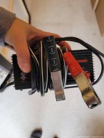 Close-up photo of battery maintainer with red and black clamps held in hand showing device details and cables.