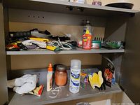 Two shelves holding assorted cleaning items such as spray bottles, gloves, cords, small cans, and jars.