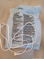 Light blue plug-in heating pad with visible warning text and white cord