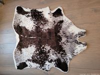 Photo of the small faux cowhide pattern rug laid on a wooden floor showing its irregular shape and color pattern.