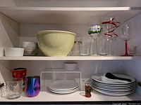 Shelf with white mixing bowl, baking dishes, various glasses (decorative and plain), plates, dipping set, and cast iron cookware