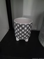 Small decorative white ceramic planter with black geometric pattern on legs, no soil or plants inside.