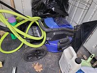 Blue and black cordless lawn mower resting on floor with garden tools nearby
