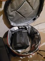 Open round soft-sided collapsible cooler showing gray and orange exterior, silver insulated interior, and black fabric bag inside.