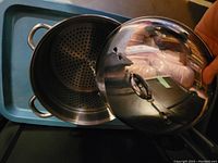 Photo showing the stainless steel steaming pot with the removable perforated steam insert and the dome-shaped lid with handle.