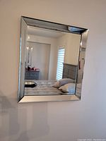 Mirror with wide beveled glass border reflecting bedroom interior