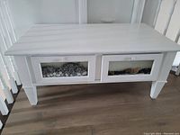 Front view of white coffee table showing two drawers with clear panels containing decorative stones and natural mix inside.
