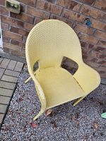 Yellow plastic outdoor chair showing wear, set on a paved surface next to a brick wall.