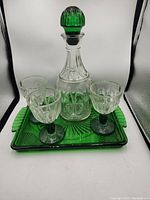 Green and clear glass decanter with stopper, three matching goblets, and a square green glass tray.