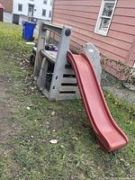 Plastic children's playset lying on its side on grass, showing red slide and beige climbing structure.