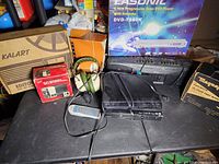 Lot of electronics including multiple DVD players, remote, headphones, and boxes displayed on a table.