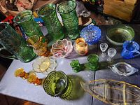 Full view of all glassware items including green Eo Brody vases, amber Murano pitcher, blue glassware, and small decorative bowls and candlesticks.