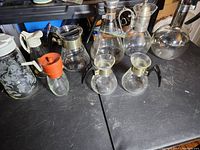 Lot of nine assorted glass carafes including some with handles and metal lids showing varied shapes and sizes