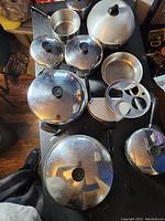 Photo showing overhead view of various Revere Ware pots and pans with lids placed on a dark surface.