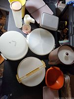 Top view of various round and rectangular Tupperware containers and lids arranged on a table, showing colors, shapes, and sizes.