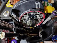Photo showing various baseball bats, a tennis racquet with cover, and part of a golf club in a container.