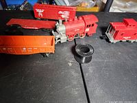 Lionel 8700 locomotive and three train cars, including an orange hopper and red boxcar, on a black surface