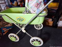 Side view of green plastic bassinet stroller body with metal frame and floral fabric canopy, displaying the Cabbage Patch Kids logo.
