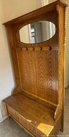 Front view of the wooden coat rack and shoe storage bench with an oval mirror and five hooks.
