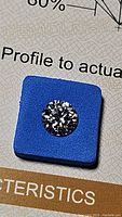 Close-up of the round 1 carat moissanite gemstone on blue holder showing facets and scintillation.
