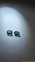 Pair of oval teal-blue sapphire gemstones under spotlight showing color and clarity.