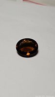 Oval dark whiskey-colored Madeira citrine gemstone resting on white background, showing high clarity and deep rich color.