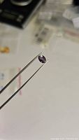Oval cut sapphire held in tweezers showing deep purple coloration under one light source.