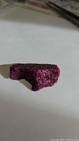 Side view of a deep red-pink natural ruby specimen showing porous honeycomb texture.