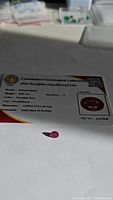 Certified natural purple red ruby with certification card showing gemological report details including weight, color, dimensions, hardness, and heat treatment indication.