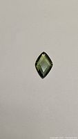 Top down photo of a single green sapphire gemstone in fancy marquise cut on a white background.