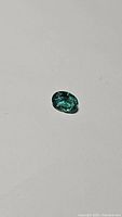 Close-up of an oval cut green emerald gemstone on a white surface.